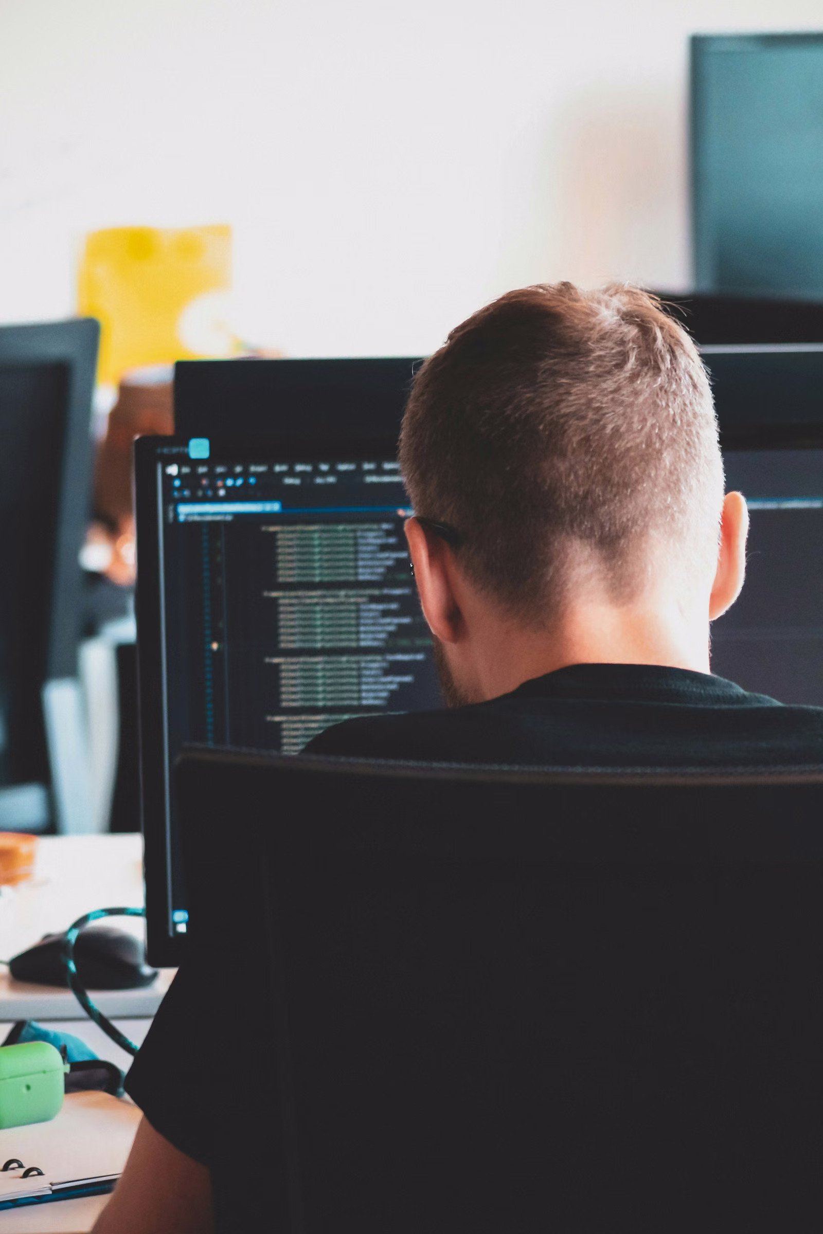 Technician viewed from behind, reviewing code on a dual-monitor workstation in an office