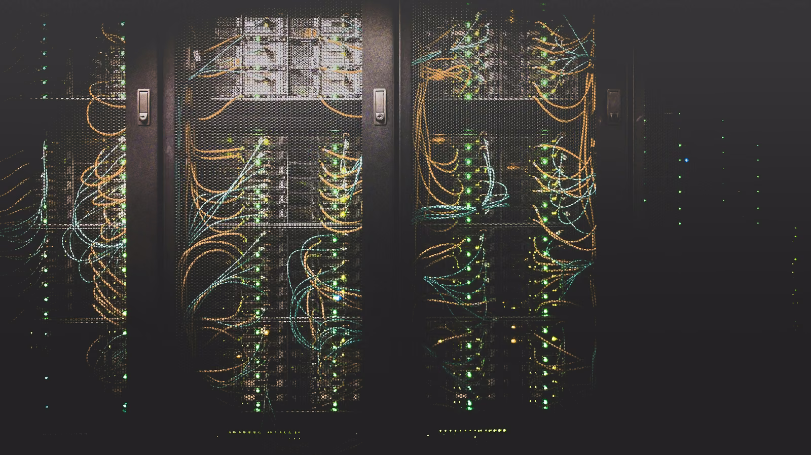 Rows of server racks with bundled orange, green and blue network cables in a dark data center
